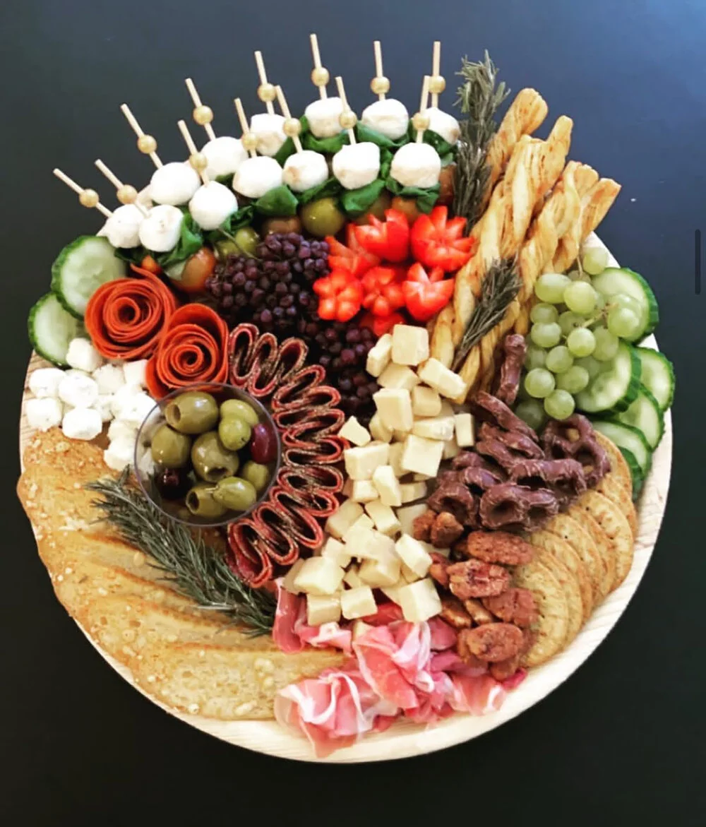 A round charcuterie board with decorative items with various meats, cheeses and fruits