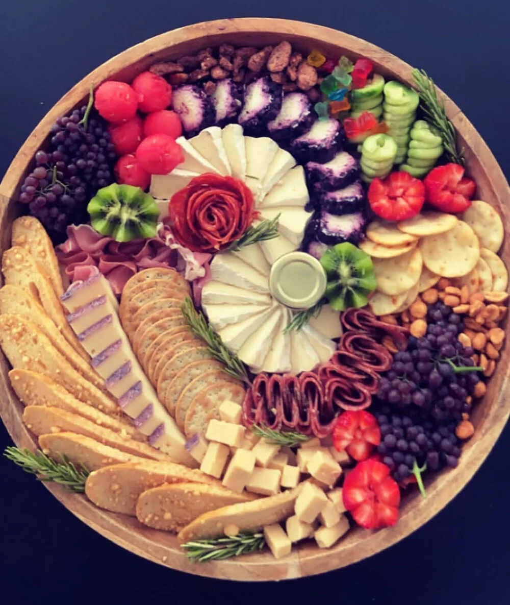 A colorful round charcuterie board filled with meats, cheeses and fruits