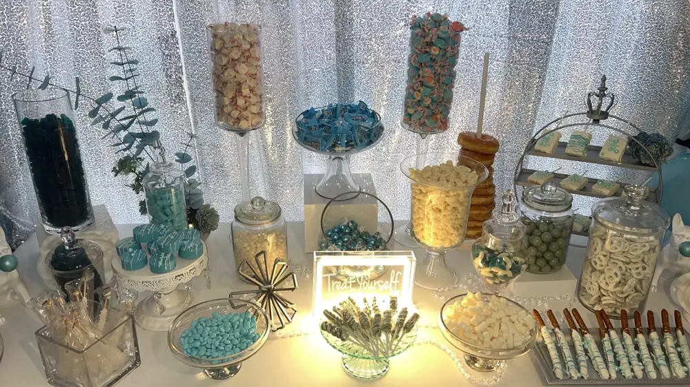 Silver party backdrop and white table with cake stands